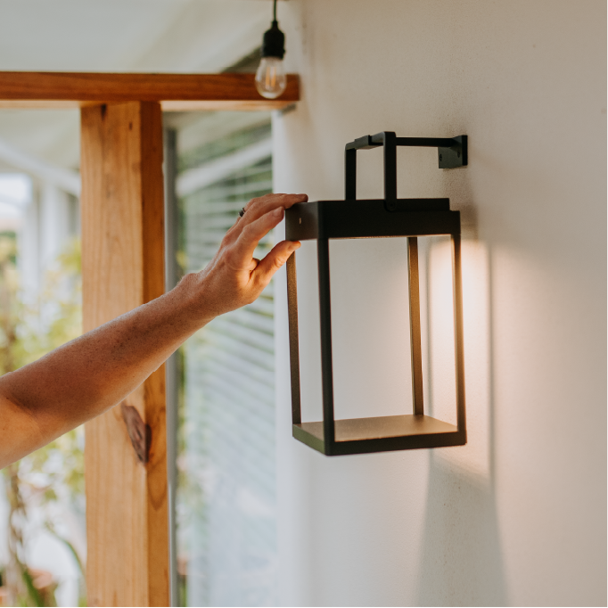 Person adjusting a wall-mounted lantern fixture on a white wall.